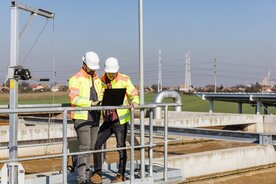 Zwei Arbeiter in Schutzausrüstung stehen mit Laptop am Klärbecken; Copyright_istock/zstockphotos